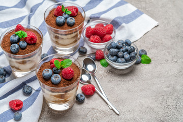 Classic tiramisu dessert with blueberries and raspberries in a glass cup on concrete background