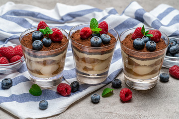Classic tiramisu dessert with blueberries and raspberries in a glass cup on concrete background