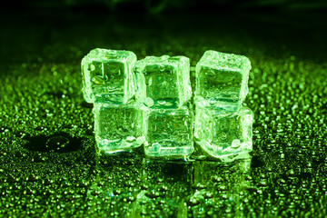 Ice cubes in green light on black wet table.