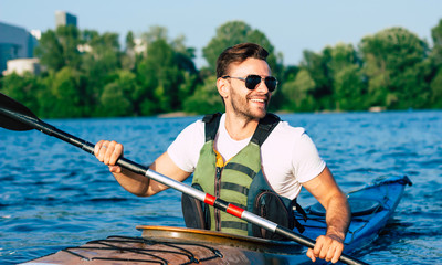 Handsome young man kayaking on a lake. Happy guy canoeing in a lake. Kayaking. Man paddling a kayak. Concept for adventure, travel, action, lifestyle