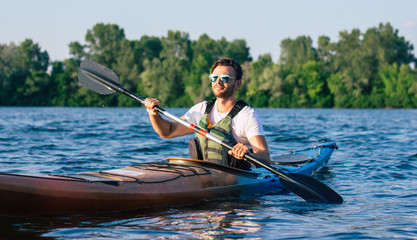Handsome young man kayaking on a lake. Happy guy canoeing in a lake. Kayaking. Man paddling a kayak. Concept for adventure, travel, action, lifestyle