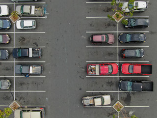 Aerial top view of parking lot at supermarket with with varieties of colored vehicles. People walking to their car and trying to park.