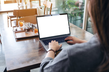 Mockup image of a woman using and typing on laptop with blank white desktop screen on wooden table
