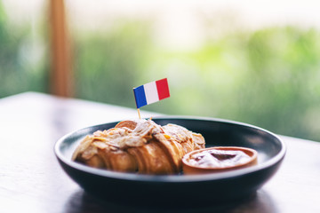 A piece of croissant and tart with a flag of France in a black plate on wooden table in cafe
