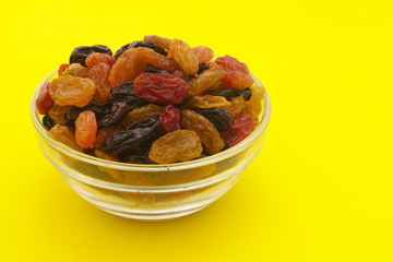 Raisins in glass bowl on yellow background