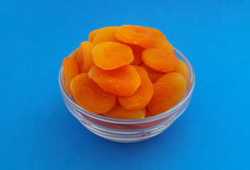 Heap of dried apricots fruits in bowl on blue background