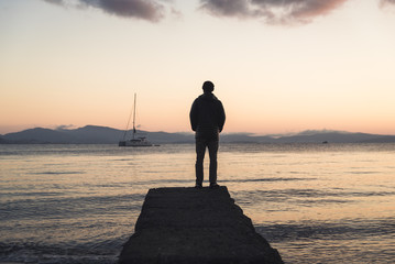 A man standing on a dock during sunrise on Kos, Greece with a boat in the background. 