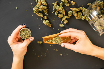 Pot use concept. Top view of marijuana blunt with grinder. Woman preparing and rolling marijuana...
