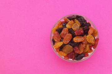 Mixed raisins in glass bowl on pink background with room for text, top view