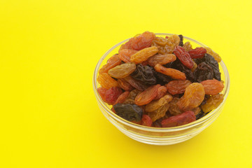 Mixed raisins in glass bowl on yellow background with copy space