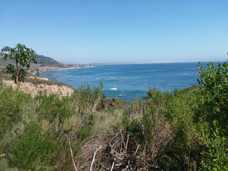 Green clifss lookind down on a rystal blue ocean, with clear blue skies