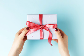 Female hands holding gift box with ribbon on blue background, top view