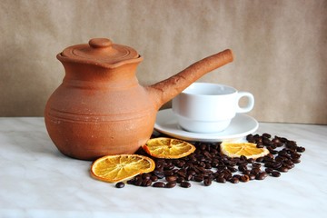 brown clay dishes, white clean Cup and saucer, roasted coffee beans and dried orange on the table, selective focus, close-up