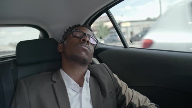 View from the inside of car of African businessman sleeping on backseat during car ride