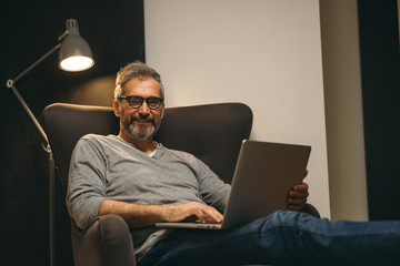 middle aged man using laptop sitting in sofa at his home