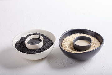 Black tahini and white tahini sauce in bowls on white background. Natural paste made from sesame seeds. Copy space.