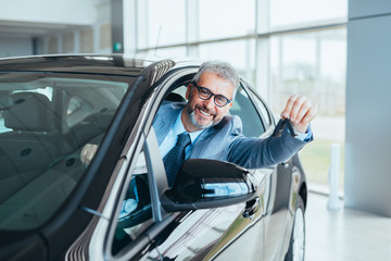 businessman sitting in car and showing car keys in car dealership showroom