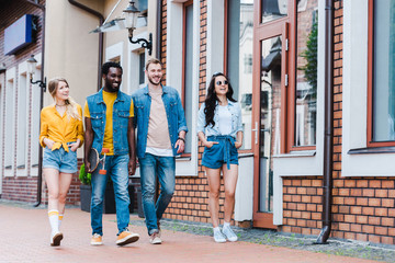 Obraz premium happy girls with hands in pockets walking with cheerful multicultural friends