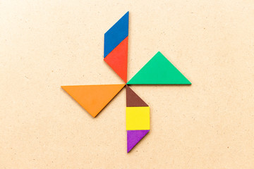 Color tangram puzzle in turbine, wheel or windmill shape on wood background
