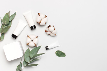 Obraz na płótnie Canvas Cosmetics SPA branding mock-up. White cosmetic bottle containers with cotton flowers, eucalyptus twigs on gray background top view flat lay. Natural organic beauty product concept, Minimalism style