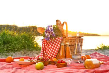 Wicker basket with tasty food and drink for romantic picnic near river