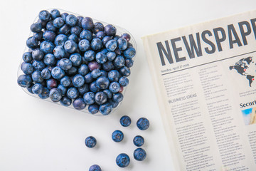 Bowl with ripe blueberry and newspaper on white background