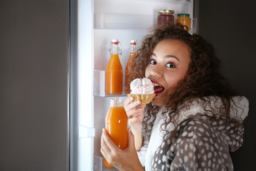 Afraid woman caught in the act of eating tasty cake near refrigerator at night