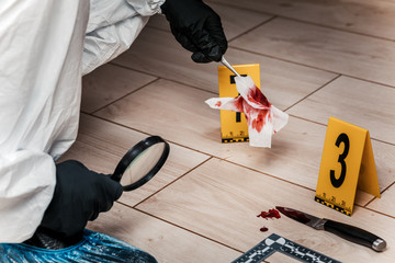 A criminology expert looks through a magnifying glass at a bloody napkin at the crime scene