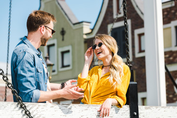 cheerful woman touching sunglasses and looking at man outside