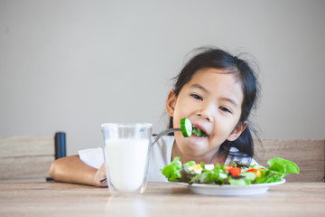 Cute asian child girl eating healthy vegetables and milk for her meal