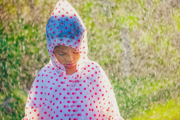 Sad asian child girl wearing raincoat standing under the rain in the rainy day