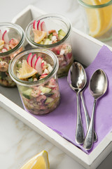 Norddeutscher Friesischer Nordseekrabben Salat Glas Becher mit Gurken, Radieschen, Zwiebeln, Dill und Zitronen auf Holz Tablett und Marmor Tisch