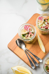 Norddeutscher Friesischer Nordseekrabben Salat Glas Becher mit Gurken, Radieschen, Zwiebeln, Dill und Zitronen auf Holz Brett und Marmor Tisch