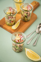 Friesischer Nordseekrabben Salat Glas Becher mit Gurken, Radieschen, Zwiebeln, Dill und Zitronen auf Holz Brett und Mint Grün Hintergrund