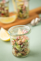 Friesischer Nordseekrabben Salat Glas Becher mit Gurken, Radieschen, Zwiebeln, Dill und Zitronen auf Holz Brett und Mint Grün Hintergrund