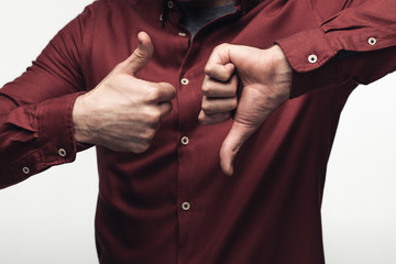 partial view of man showing thumb up and thumb down isolated on grey, human emotion and expression concept