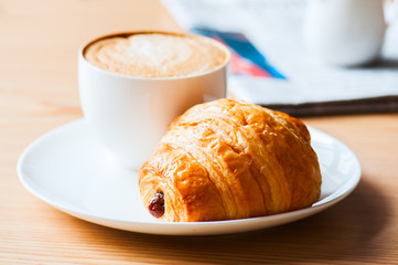 One cup of coffee and croissant on a white plate