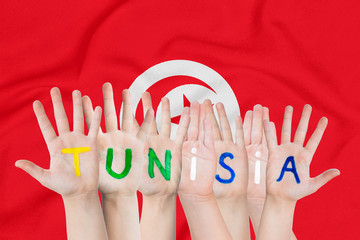 Inscription Tunisia on the children's hands against the background of a waving flag of the Tunisia