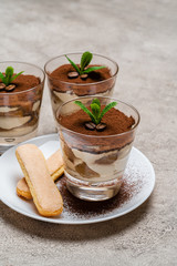 Classic tiramisu dessert in a glass cup and savoiardi cookies on plate on concrete background