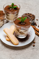 Classic tiramisu dessert in a glass cup and savoiardi cookies on plate on concrete background