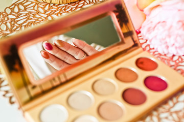 Swatches of colorful eyeshadows on the females fingers in reflection of a palette mirror.