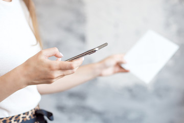 Girl holds and touching the screen of the smartphone is typing text for a message is checking the mail is stretched by a white envelope