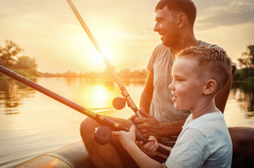 Happy Father and Son together fishing from a boat at sunset time