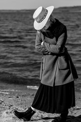 The girl on the shore of the reservoir in a straw hat and coat. Black and white photography.