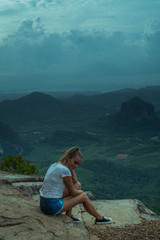 Naklejka premium Woman taveler sitting on the cliff and looking at the beautiful landscape with mountains and valley with cloudy morning sky