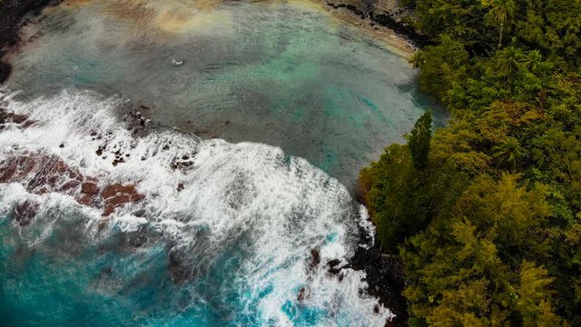 aerial cinemagraph of shipman beach in puna hawaii, a secluded cove that requires a good hike to get there. but the black and white sand mix with the clear water is worth it.