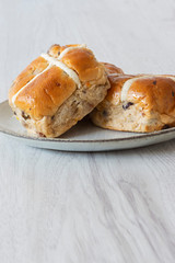 Hot cross buns piled on a green glazed plate with a grey wood background