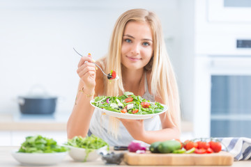 Obraz na płótnie Canvas Young happy blonde girl eating healthy salad from arugula spinach tomatoes olives onion and olive oil