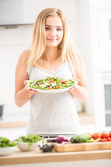 Young happy blonde girl eating healthy salad from arugula spinach tomatoes olives onion and olive oil