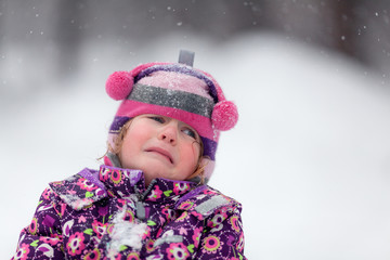 Portrait of a sad girl in a winter park. The baby is crying.